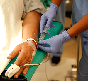 Closeup of healthcare provider injecting medication into IV port in man's hand.